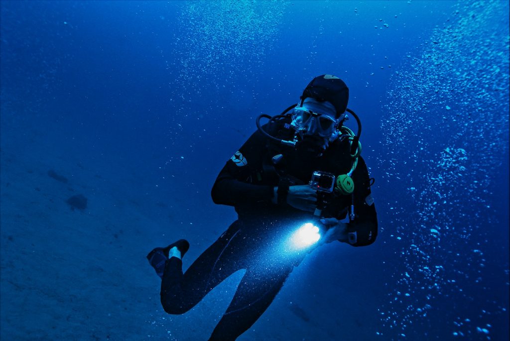 Diver holding a flashlight underwater in dark blue water